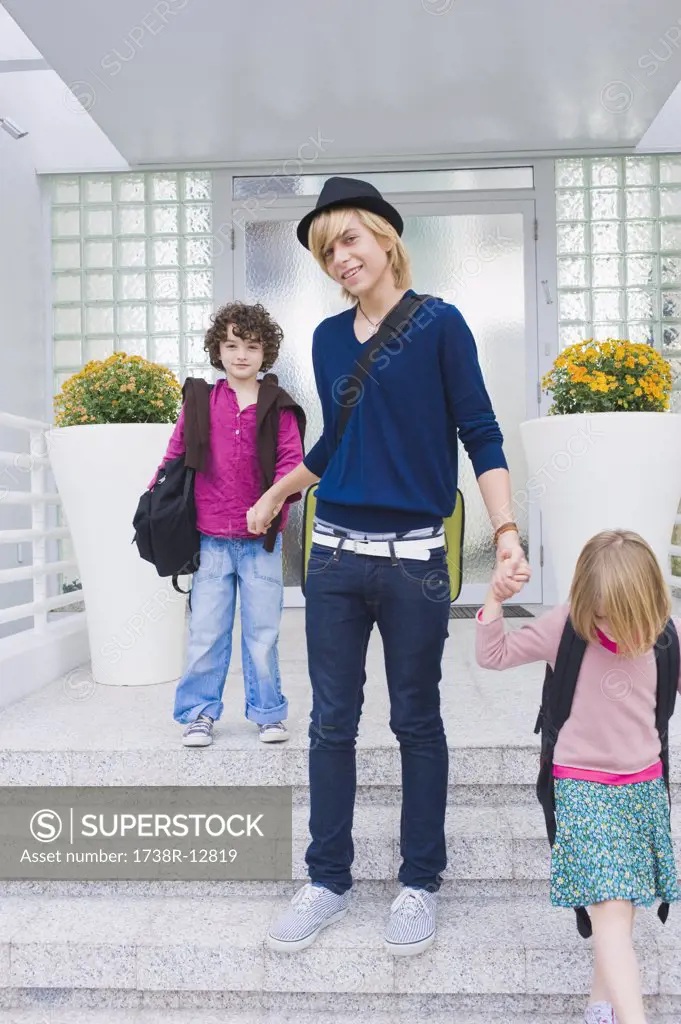 Teenage boy holding hands of schoolchildren