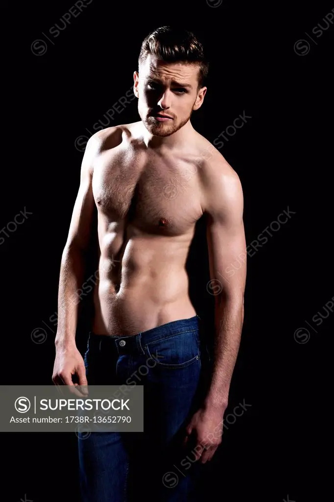 Topless man, black background; wearing jeans, serious, frowning, on arm alongside his body