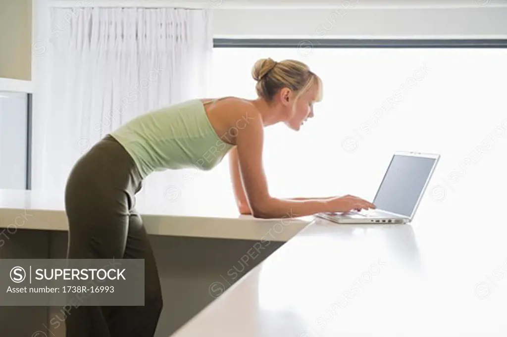 Woman leaning on a counter and working on a laptop