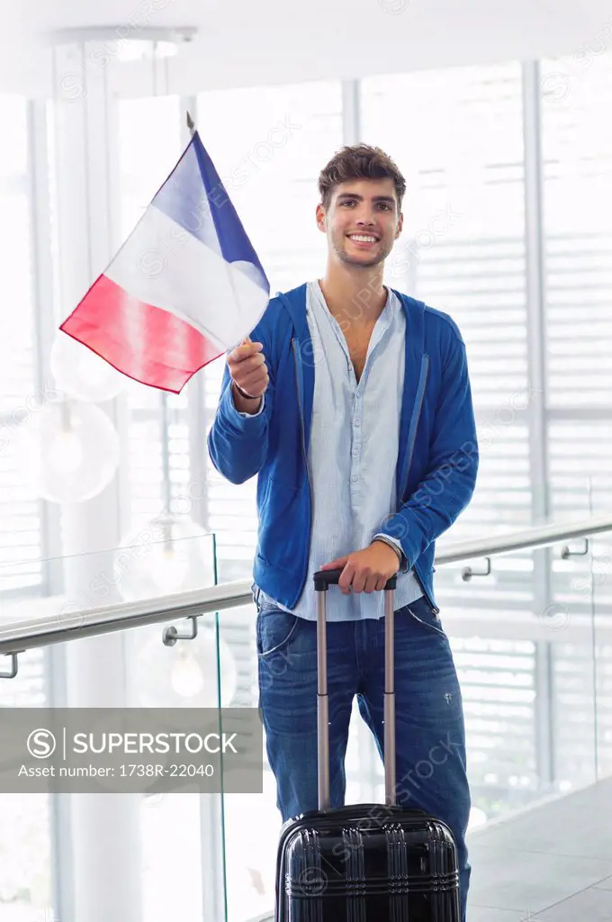 Portrait of a man holding French flag and a suitcase at an airport