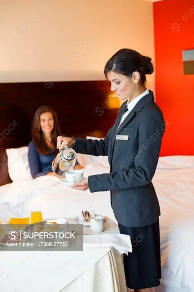 Waitress serving tea to a woman in a hotel room