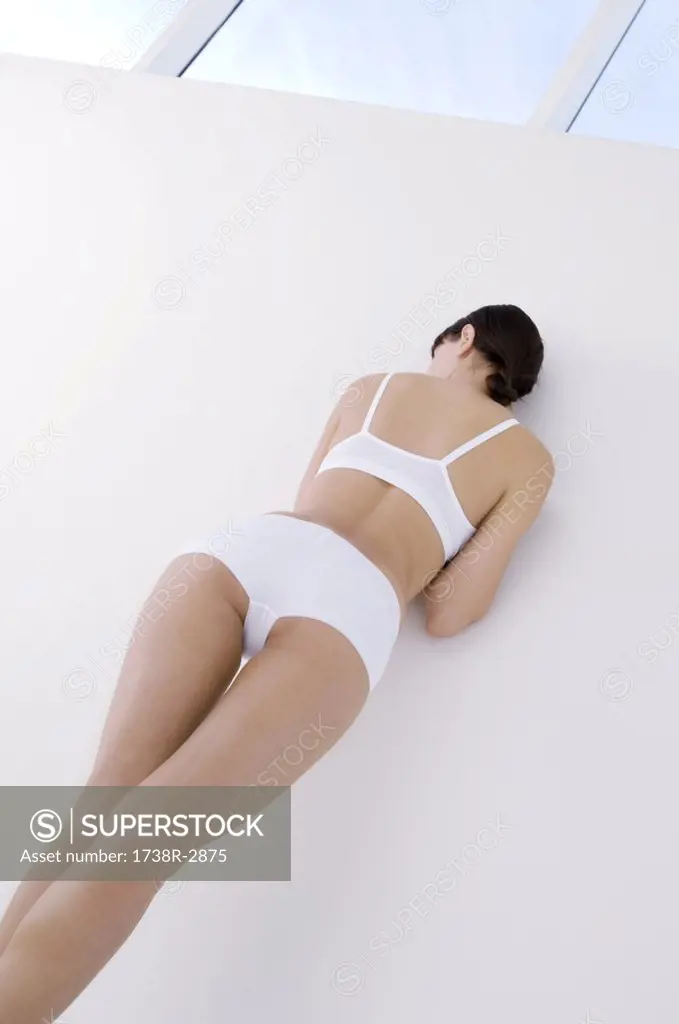 Young woman in underwear, leaning against wall - SuperStock
