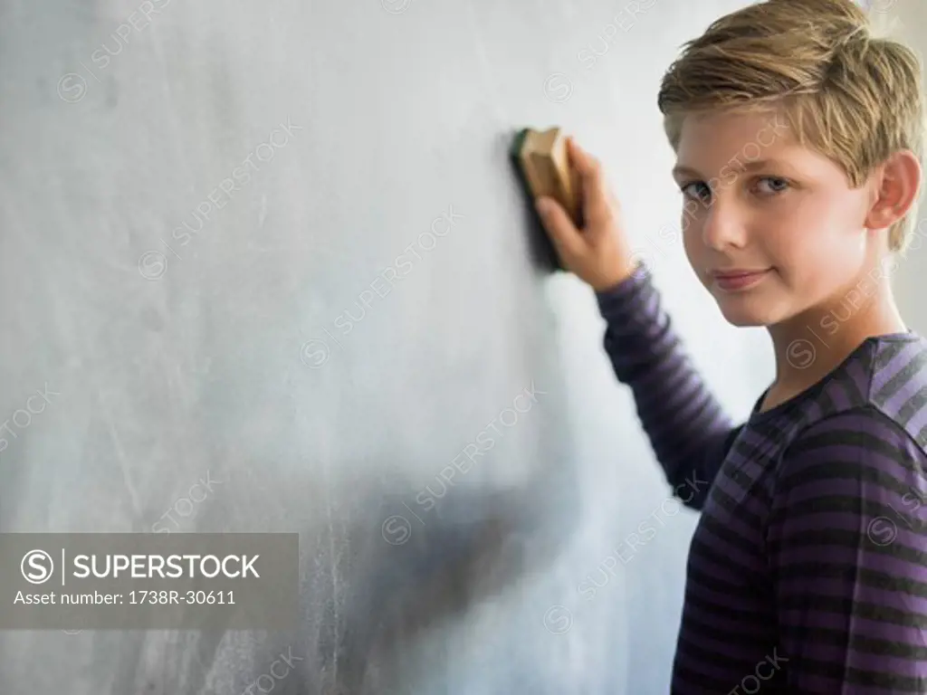 Boy cleaning blackboard with a duster in a classroom