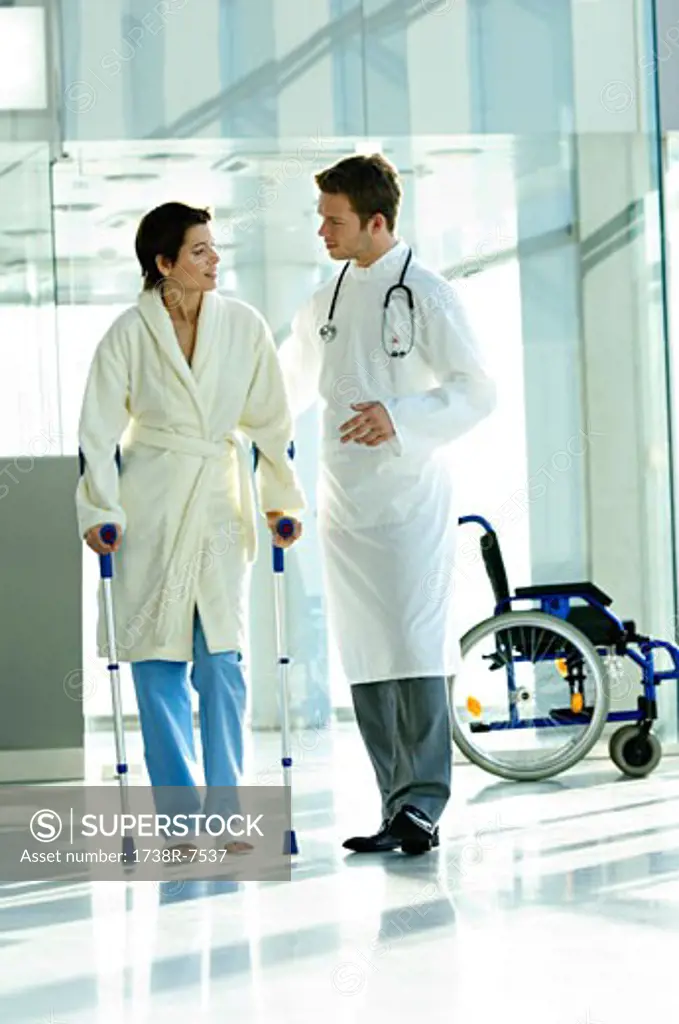 Male doctor assisting a female patient in walking on crutches