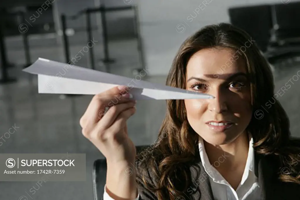 Young businesswoman holding paper airplane in airport.