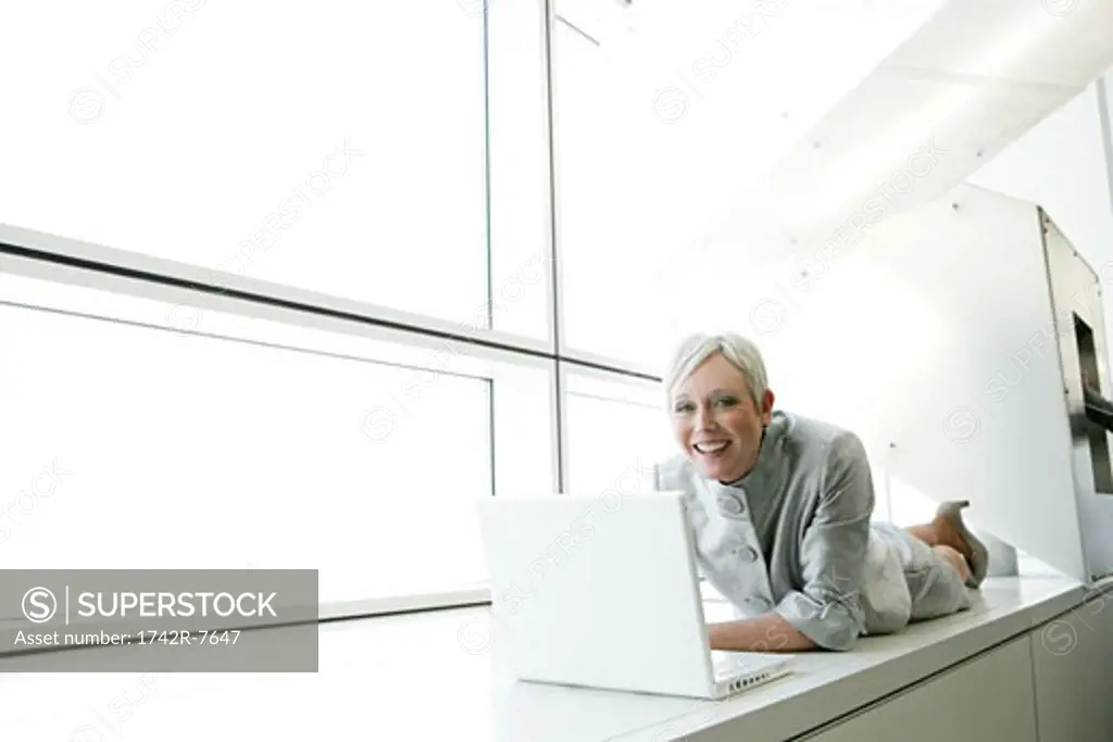 Happy mature woman relaxing in airport with laptop.