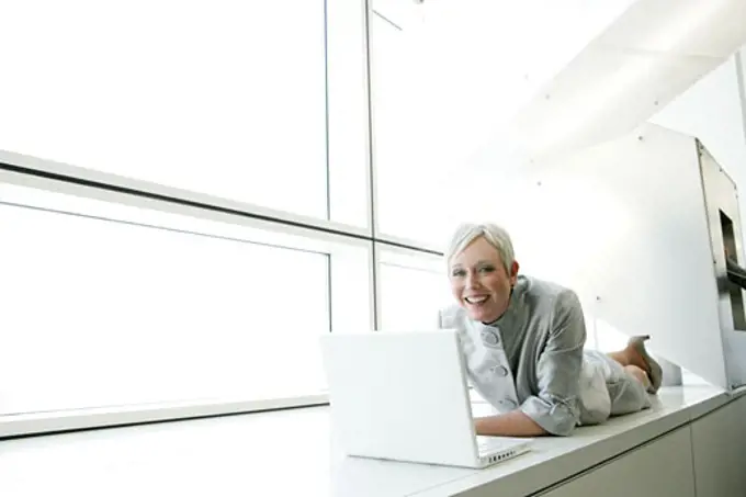 Happy mature woman relaxing in airport with laptop.