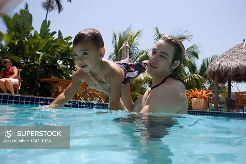 Young man holding his son in a swimming pool