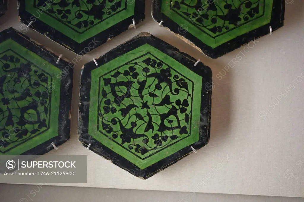 Hexagonal tiles painted with black cruciform arabesque scrolls and blossoms. From Iran. Dated 15th Century