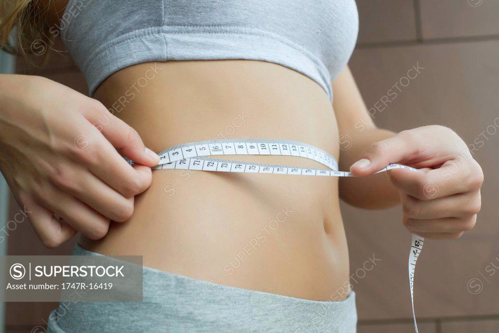 Woman measuring waist with tape measure - SuperStock