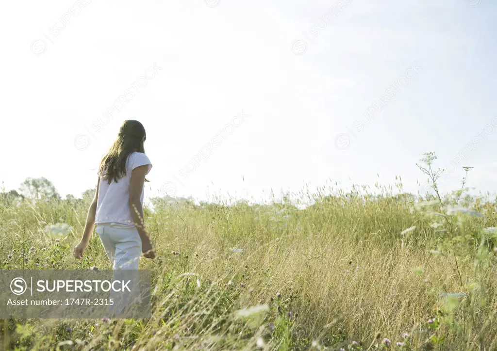 Girl walking through tall grass in field