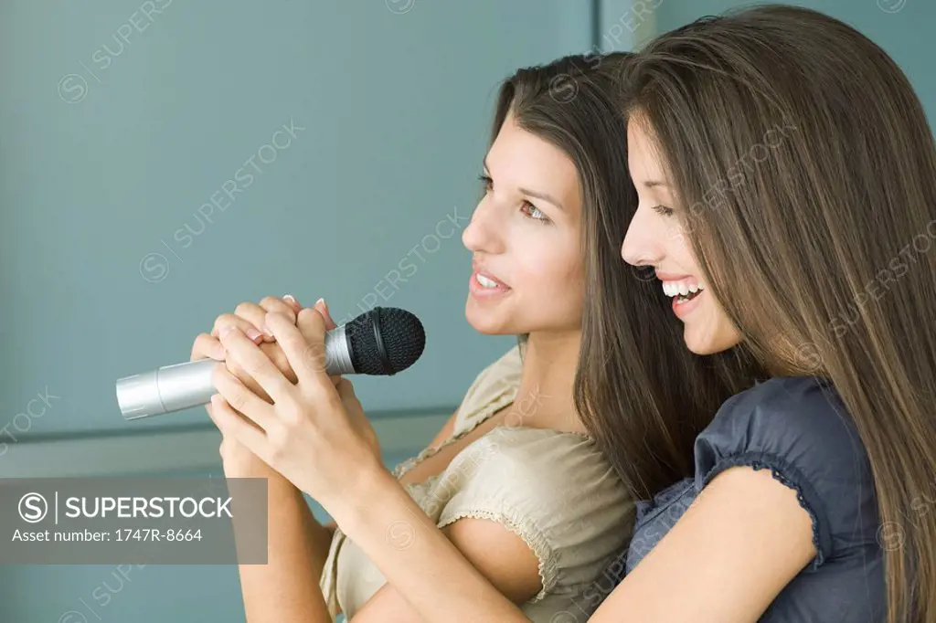 Teenage twin sisters singing into microphone together, side view