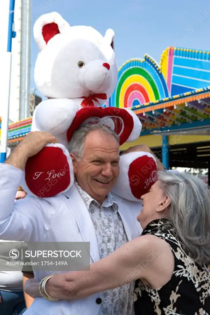 Senior man holding a stuffed animal with senior woman hugging him