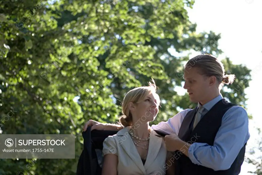 Young man putting his coat around a young woman's shoulders