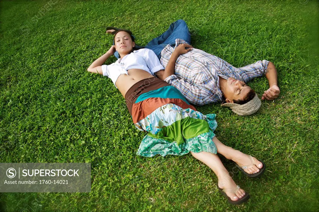 Hawaii, Kauai, North Shore, Young couple take a nap in grass.