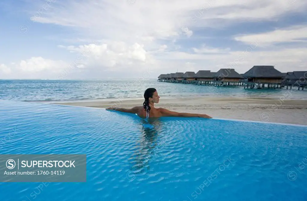 French Polynesia, Moorea, Woman relaxing in resort pool, Luxury resort bungalows in background.