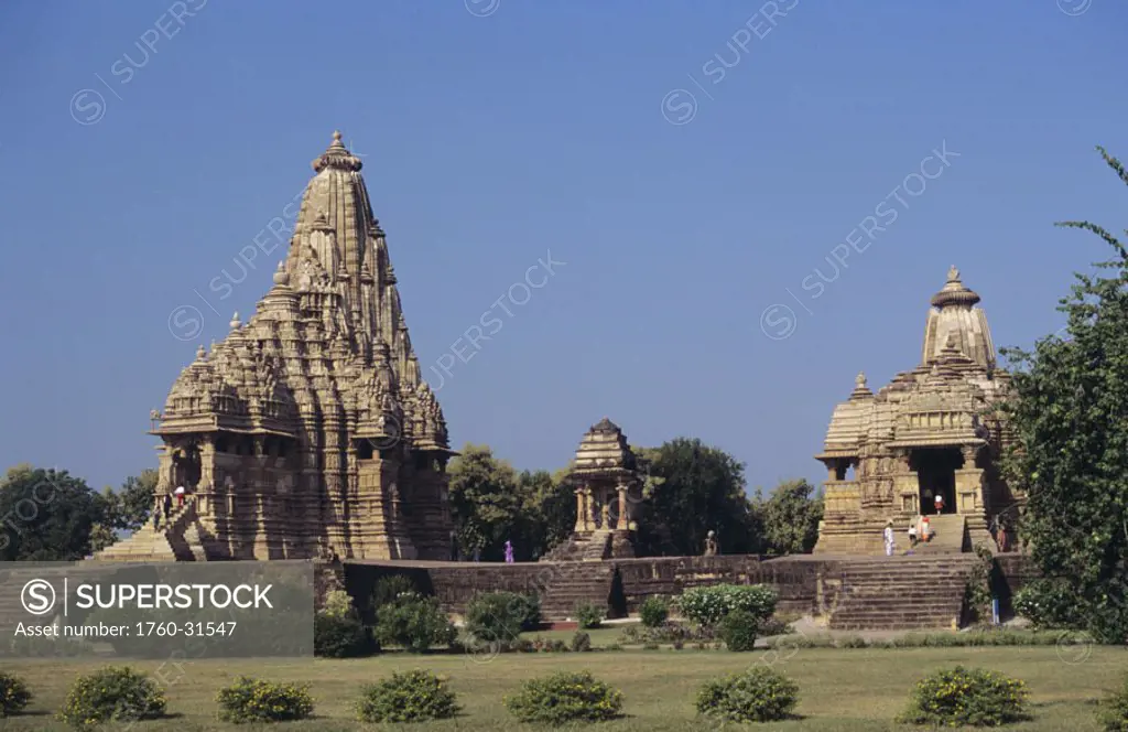 India, Khajuraho, Kandariya Mahadev and Devi Jagadamba temples among greenery, clear blue sky.