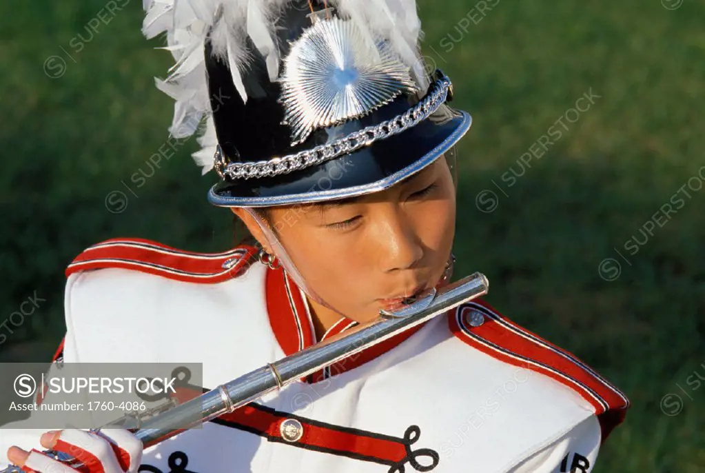 Young Asian girl in band costume playing flute, close-up headshot