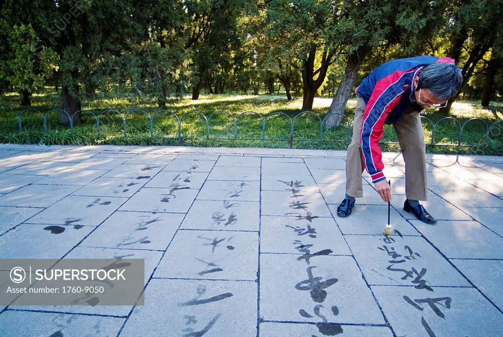 China, Beijing, An elderly Chinese man paints Taosist writings Chinese Calligraphy in water near The Temple of Heaven.