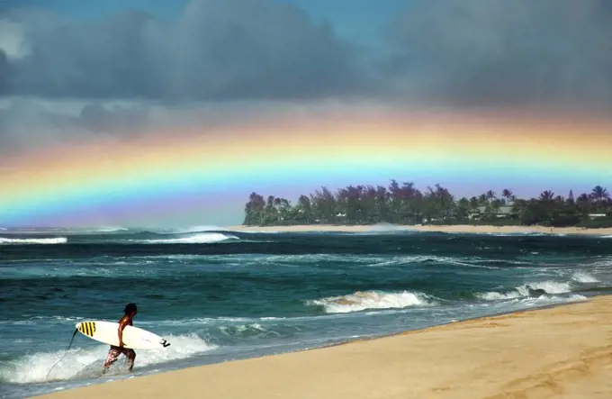 Hawaii, Oahu, North Shore, Surfer exiting water admires a beautiful, bright rainbow. Editorial Use Only.