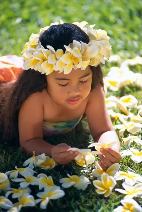 Closeup of little Hawaiian girl laying on grass with plumeria flowers C1460