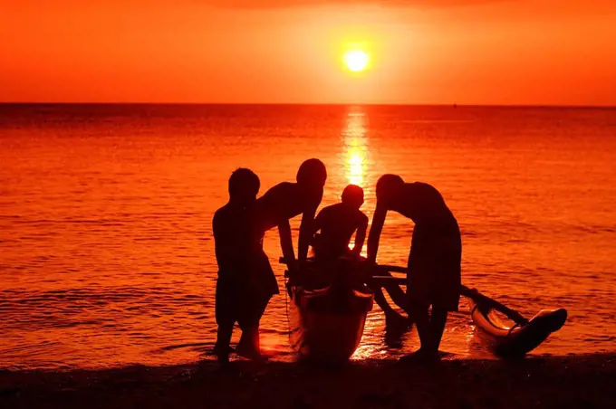 Hawaii, Oahu, North Shore, group of boys hold a canoe, silhouetted by bright orange sunset 