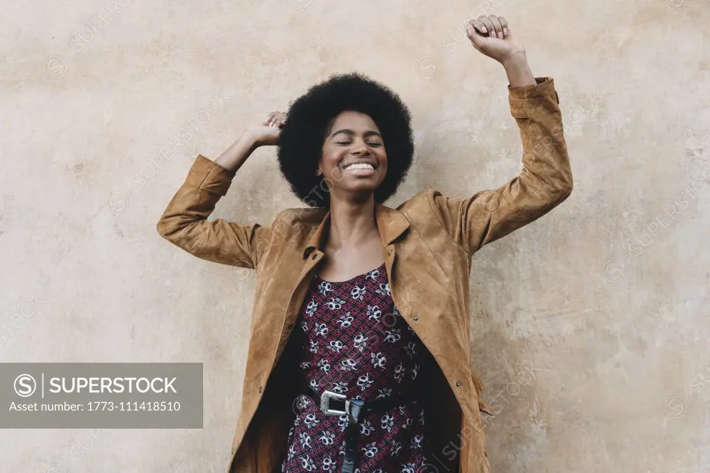 Young woman with afro hair feeling excited against stone wall