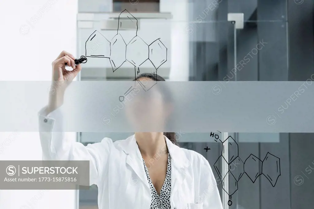 Medical student drawing atoms on glass wall in classroom