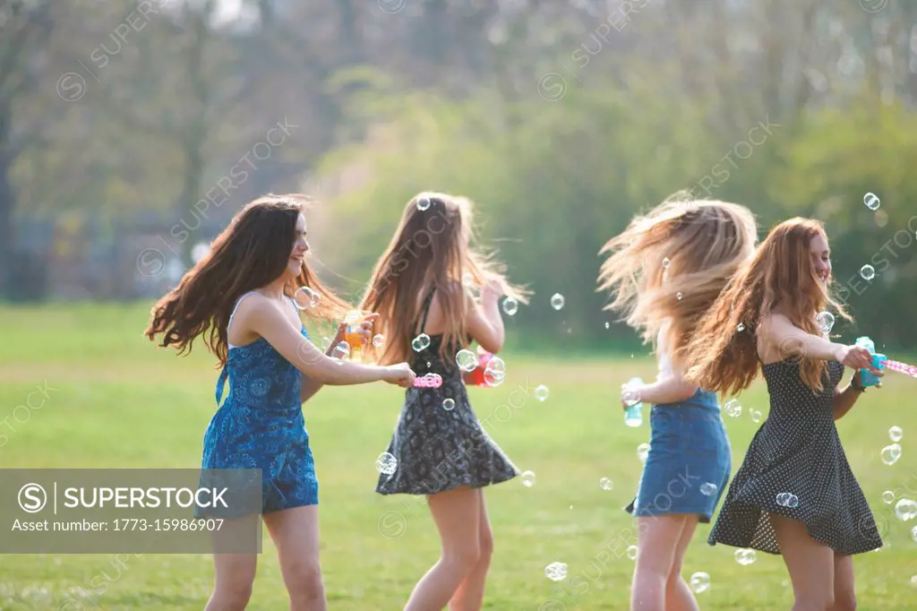 Four teenage girls spinning bubbles with bubble wand in park