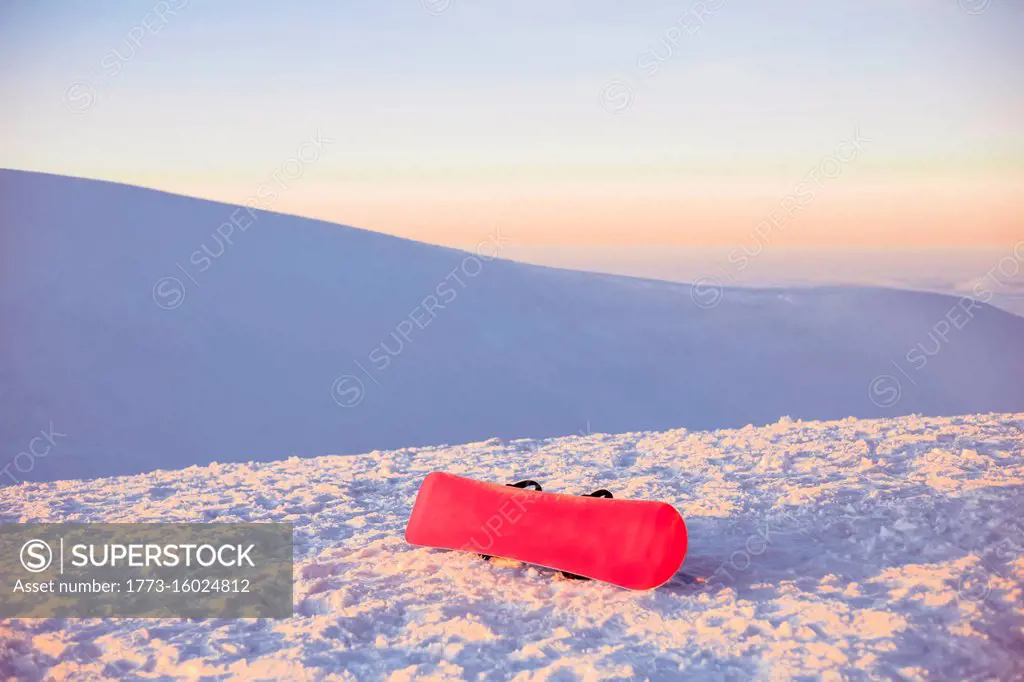 A red snowboard on a snowy slope at sunset