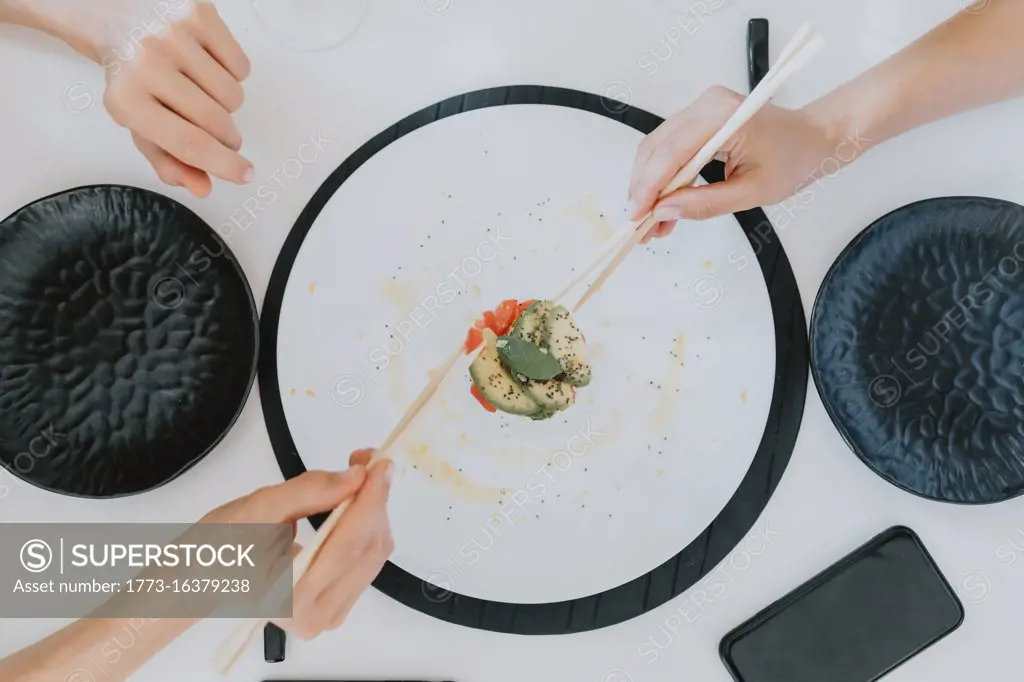 High angle close up of two women sitting at a table, eating sushi.