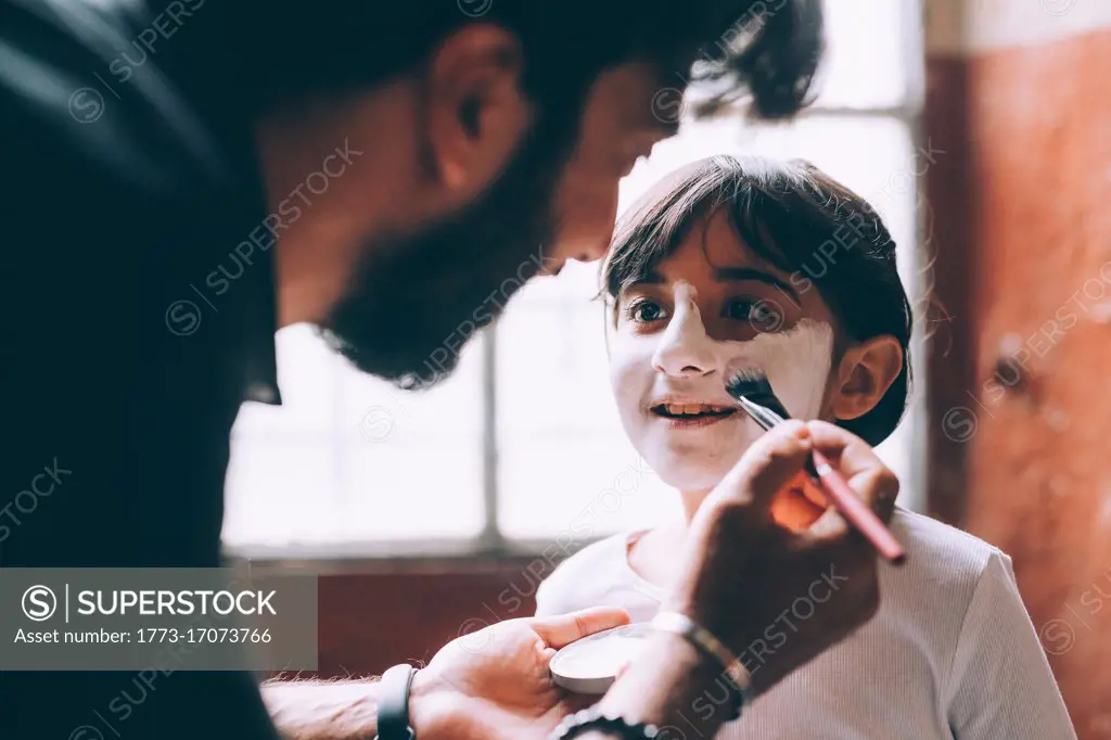 Father painting daughter's face for Halloween