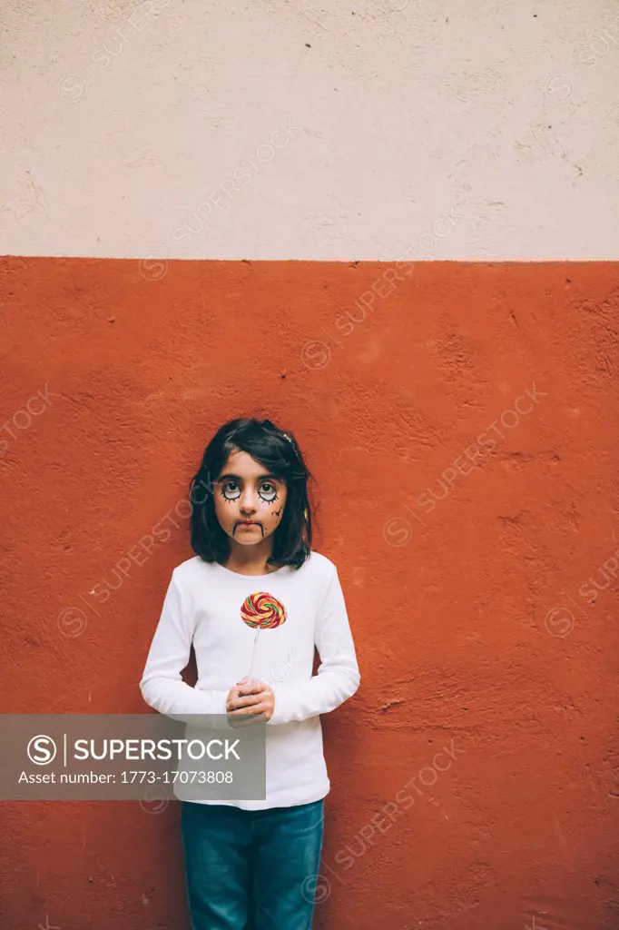 Girl with Halloween face paint, holding lollipop