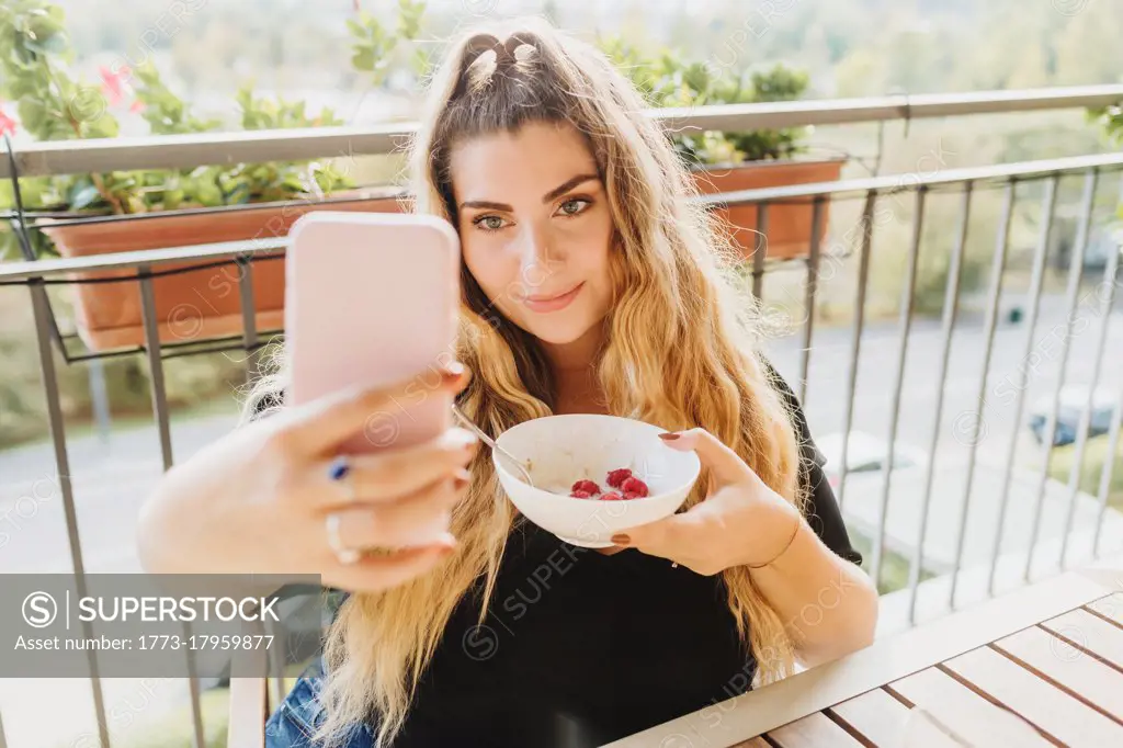 Young woman taking selfie with healthy breakfast bowl