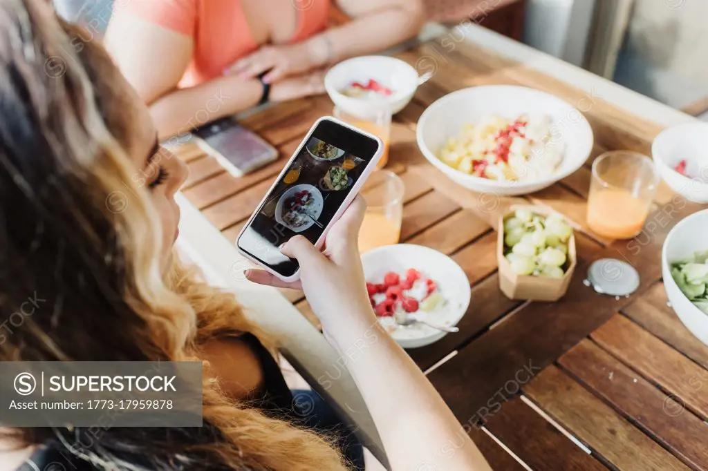 Young woman taking picture of healthy breakfast