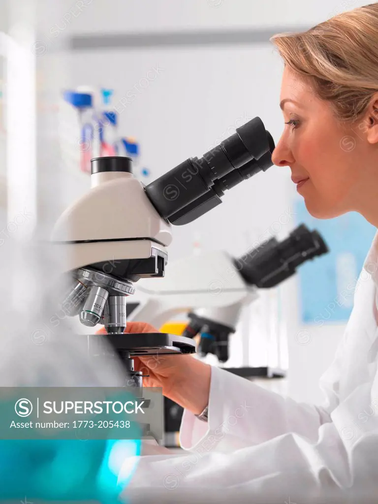 Female microbiologist viewing specimen under microscope in lab