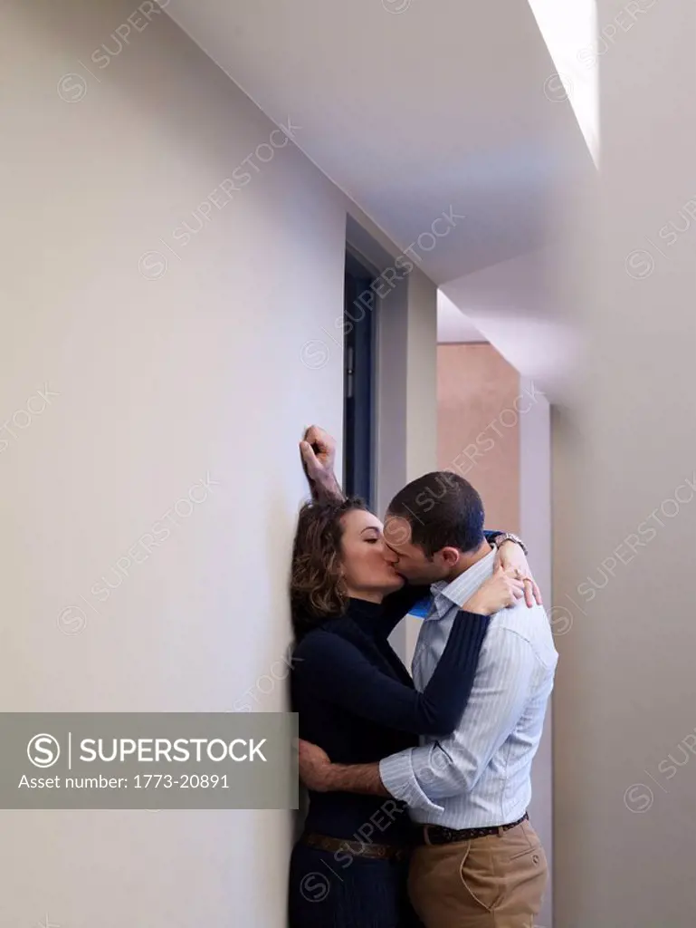 Young couple kissing in the middle of the office corridor. - SuperStock