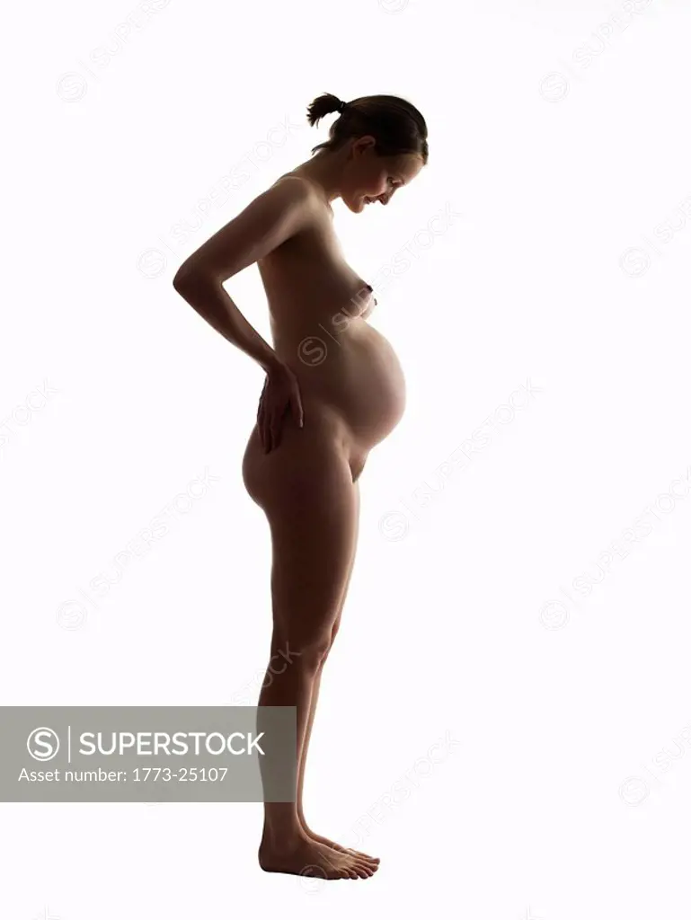 Silhouette of nude pregnant woman looking down at her stomach. Profile  view. - SuperStock