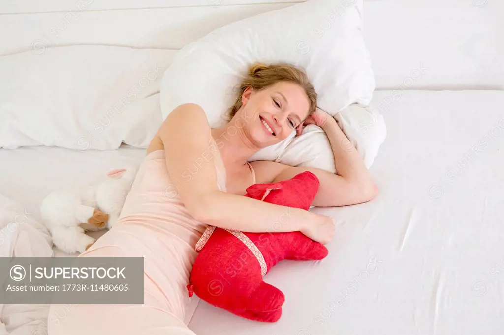 Mid adult woman lying on bed holding soft toy