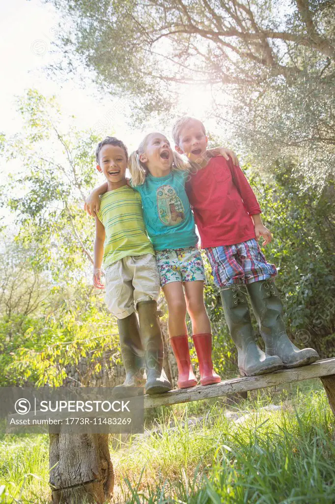 Three children standing on garden seat with arms around each other