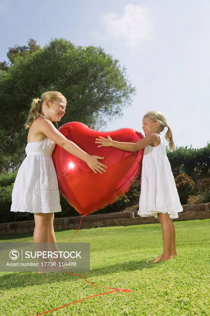 Young girls hugging red heart balloon