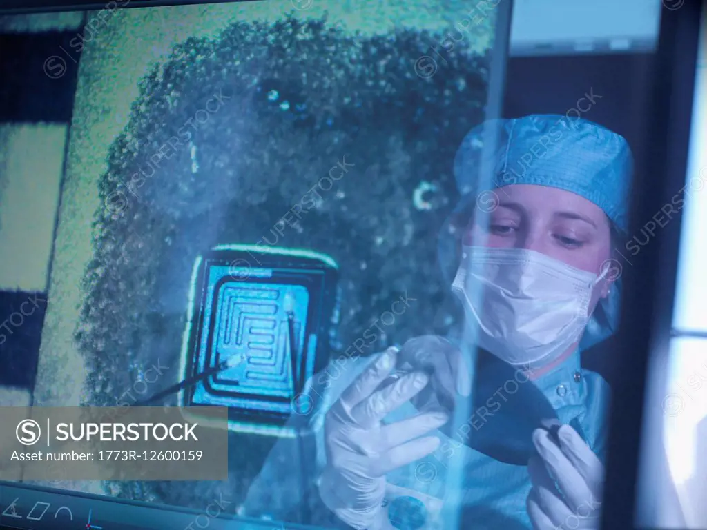 Electronics worker holding silicon wafer reflected in screen in clean room