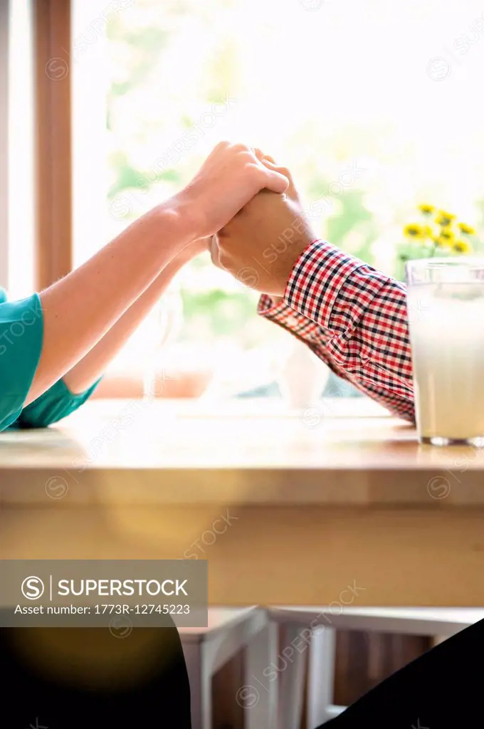 Cropped shot side view of couple holding hands across table