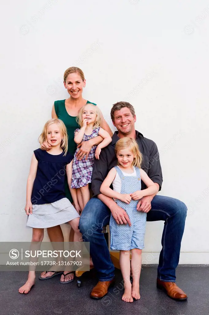 Family portrait of parents and three young daughters in front of white wall