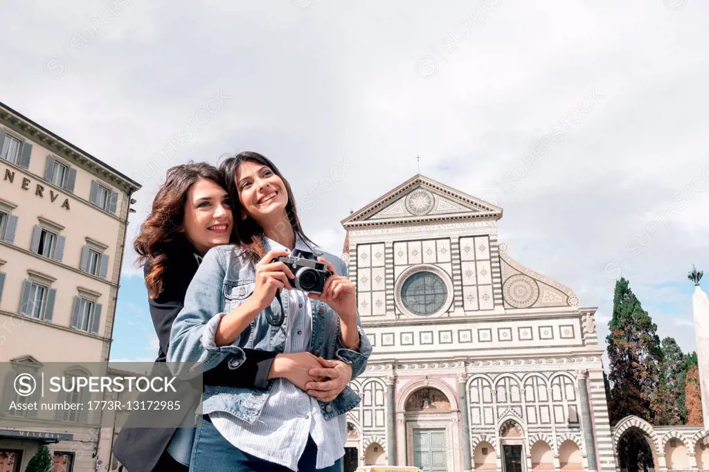 Lesbian couple holding digital camera hugging in front of church, Piazza Santa Maria, Novella Florence, Tuscany, Italy