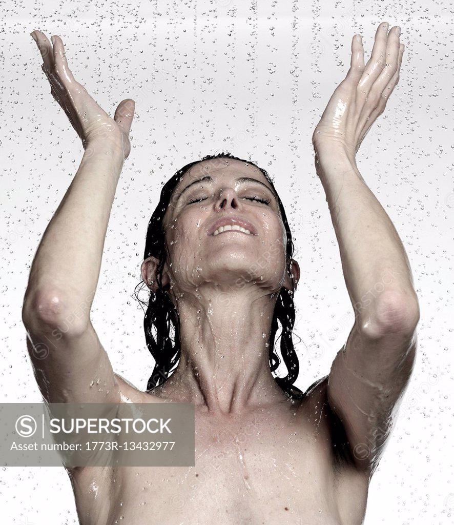 Naked mature woman showering with hands raised - SuperStock