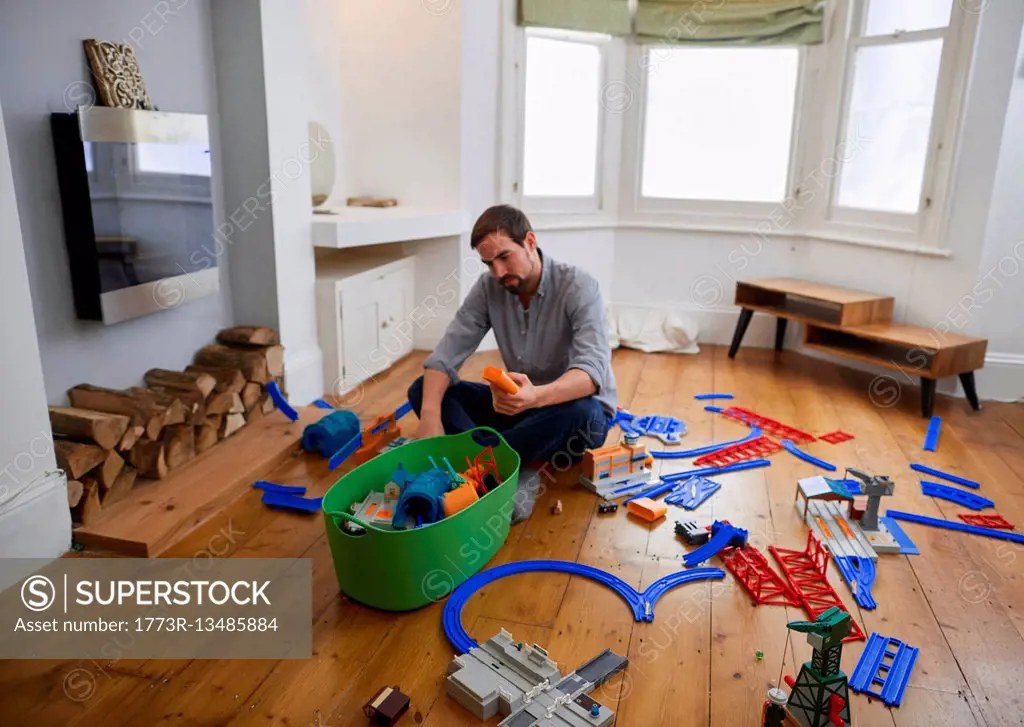 Mid adult man contemplating toys scattered in living room SuperStock