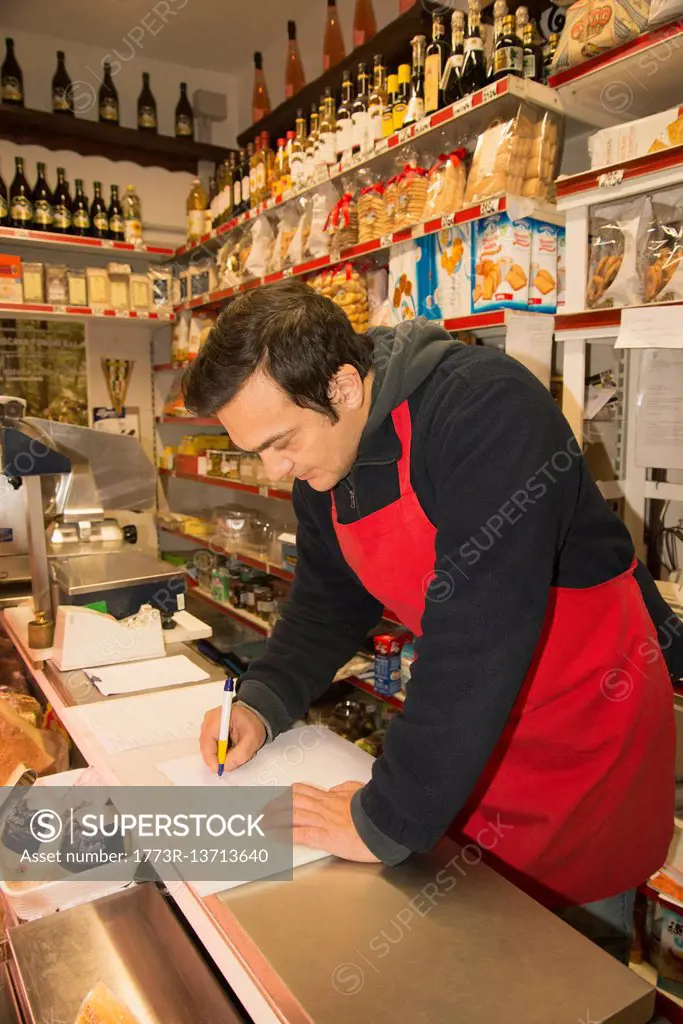 Mature male grocer writing notes in local italian grocery shop