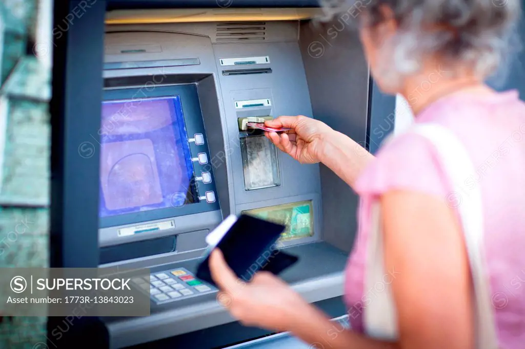 Mature woman inserting credit card into local french cash machine