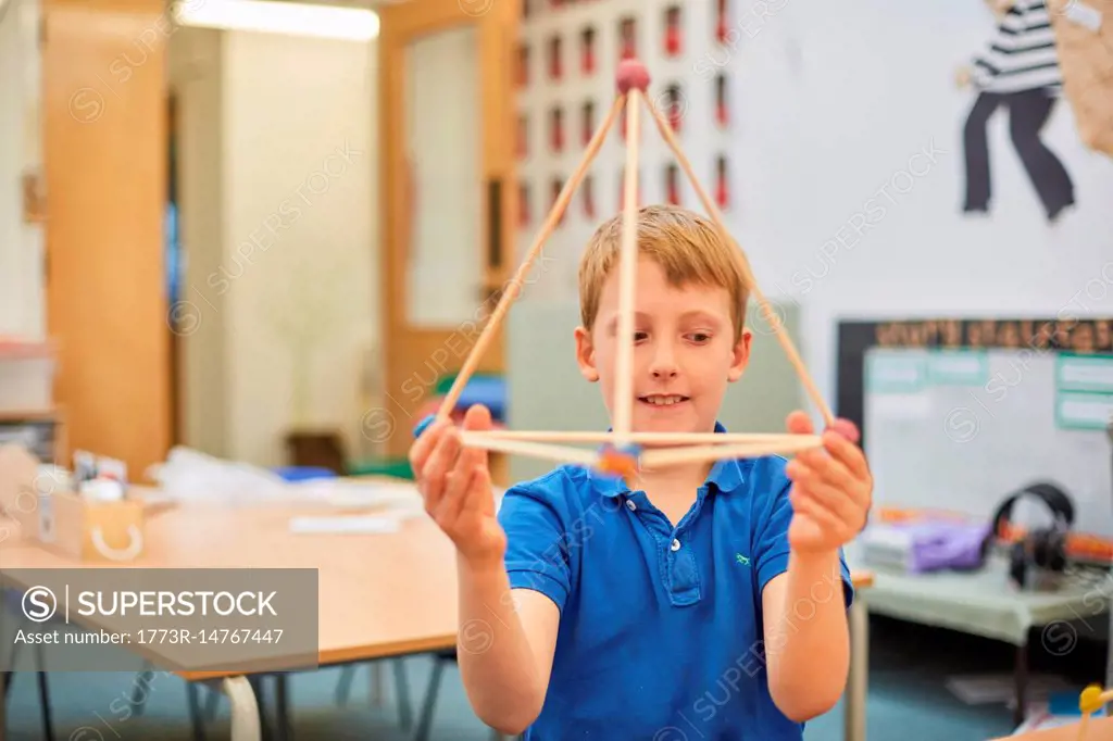 Primary schoolboy holding up plastic straw pyramid in classroom